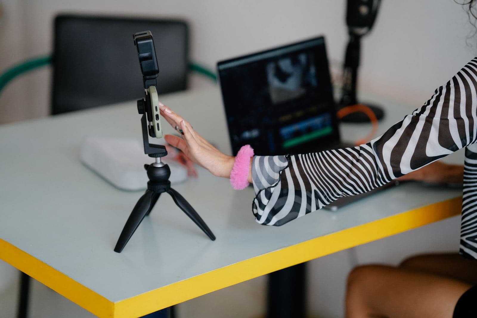 Woman adjusting a smartphone on a tripod with a laptop beside it, a typical setup for short social videos